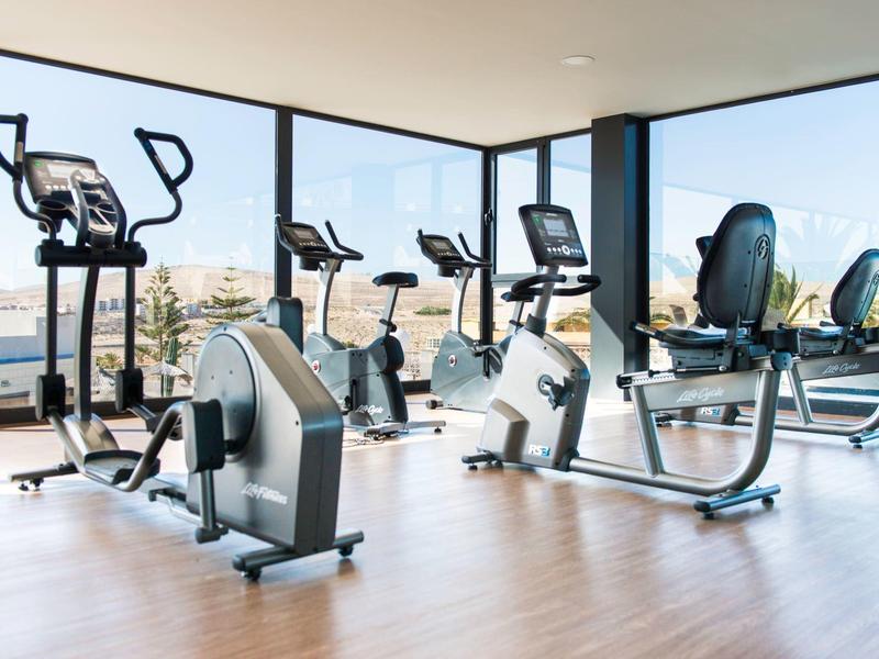 Palestra luminosa con cyclette e macchine ellittiche vicino a grandi finestre con vista sull'oceano.