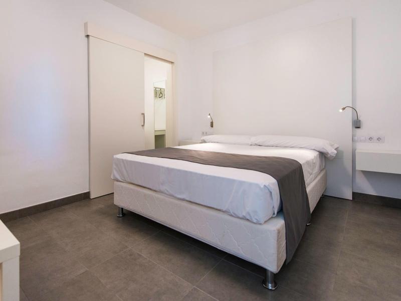 Camera d'albergo minimalista con letto matrimoniale, pareti bianche e pavimento grigio.