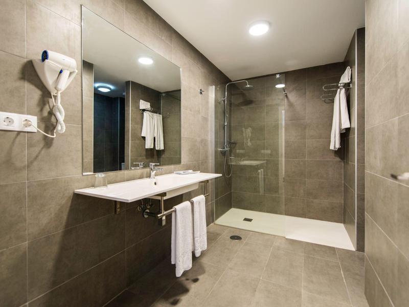 Bagno moderno in hotel con grande specchio, doppi lavandini e doccia a filo in vetro.