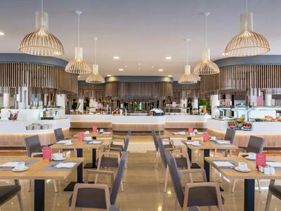 Ristorante d'hotel moderno con tavoli in legno, comode sedie e lampade a sospensione decorative.