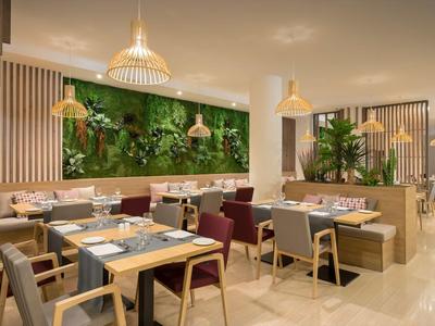 Modern hotel dining area with wooden tables, cushioned chairs, and a vertical garden wall.