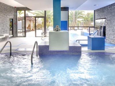 Indoor pool area with clear water, stone walls, blue accents, and glass doors leading outside.
