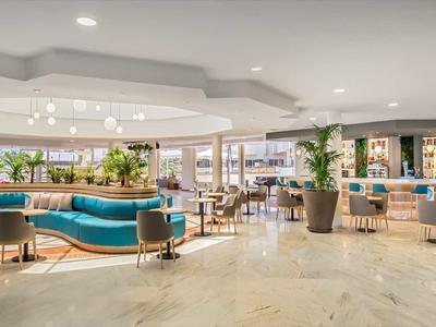 Großer, heller Lobbybereich mit blauen Sitzbänken, Pflanzen und Holzfußboden.