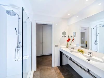Bright modern bathroom with shower, long mirror, double sinks, and brown tiled floor.