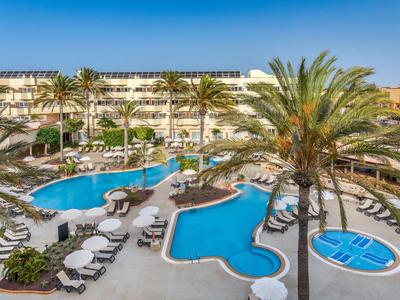 Outdoor hotel pool area with palm trees, sun loungers, and a backdrop of modern building.