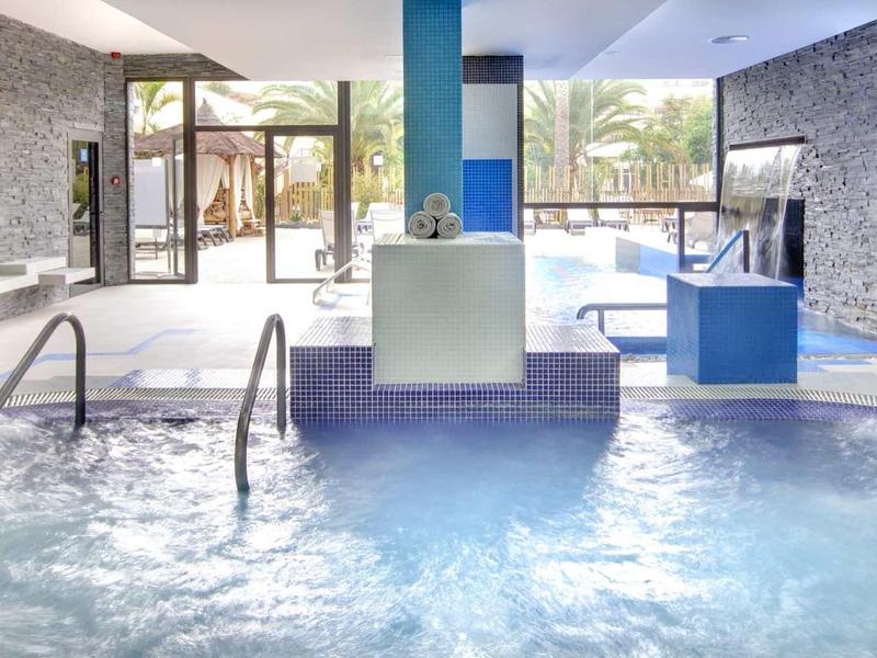 Indoor pool area with clear water, stone walls, blue accents, and glass doors leading outside.