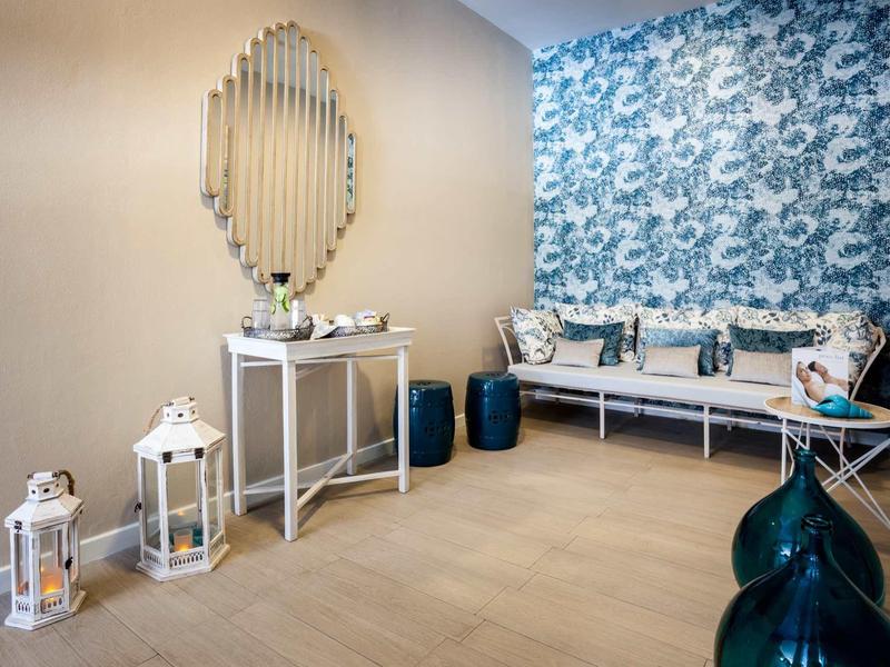 Modern hotel lobby with floral wallpaper, wall mirror, lanterns, and seating area with cushions.
