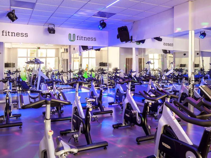 Spacious gym with rows of stationary bikes under bright ceiling lights and mirrored walls.