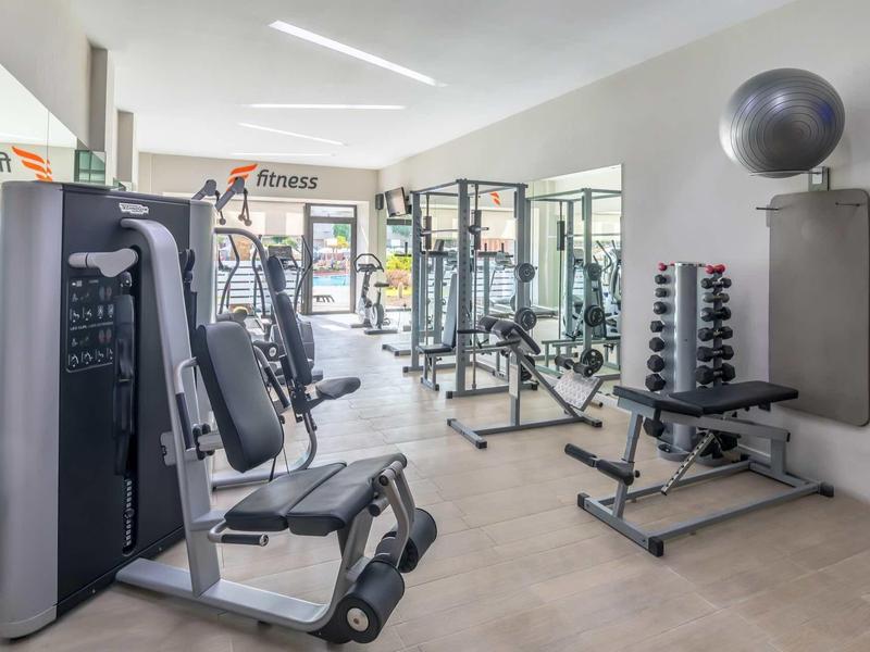 Modern hotel gym with weight machines, dumbbells, and yoga ball in bright room.