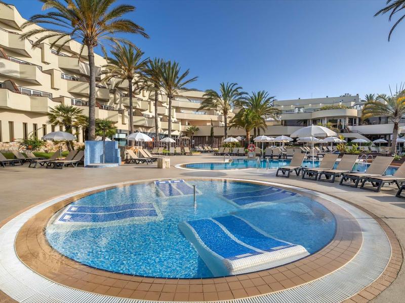 Curved outdoor hotel pool with lounge chairs and palm trees under a clear blue sky.