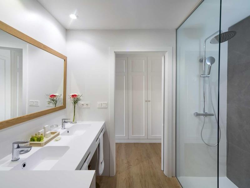 Modern hotel bathroom with a double sink, large mirror, and glass shower enclosure.