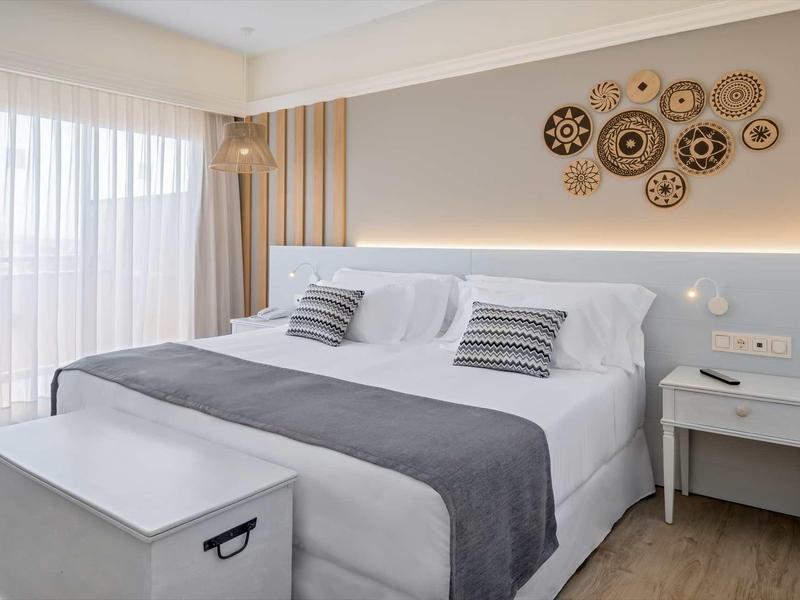 Bright hotel room with a king bed, gray and white linens, nightstands, and decorative wall art.