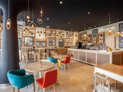 Moderní kavárna s barevnými židlemi, stoly a dobře osvětleným barem v pozadí.