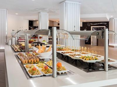 Modern buffet with various dishes including salads, sandwiches, and desserts in a bright dining area.