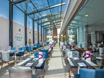 Bright, spacious hotel restaurant with glass ceiling, colorful chairs, and neatly set tables.