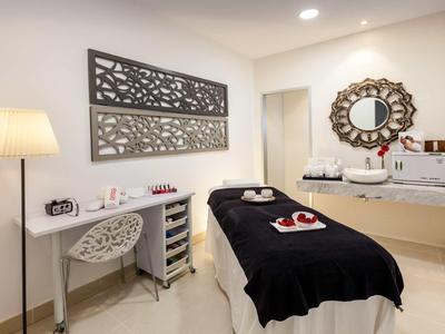 Modern spa room with massage table, decorative mirror, and a desk with chair and lamp.
