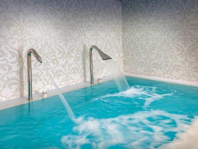 Indoor pool with water fountains flowing from two silver spouts into blue water.