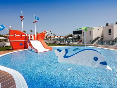 Outdoor hotel pool with marine-themed slide and whale-shaped water feature under clear blue sky