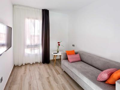 Small living space with gray sofa, colorful pillows, a round wooden table, and wall-mounted TV.