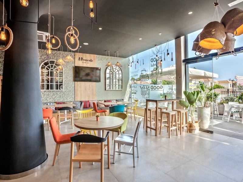 Bright, modern hotel cafe with colorful chairs and large windows opening to an outdoor seating area.