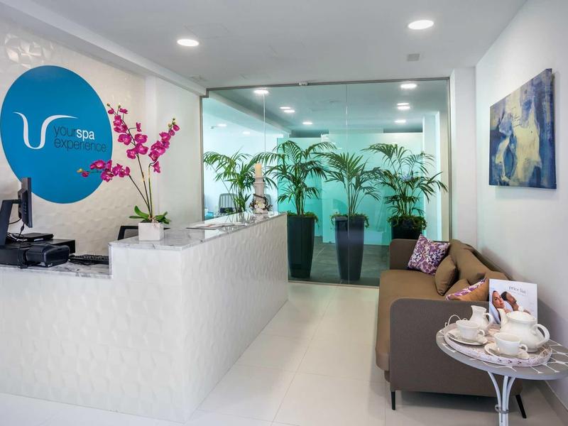Bright hotel lobby with white textured reception desk, orchid, brown sofa, and green plants.