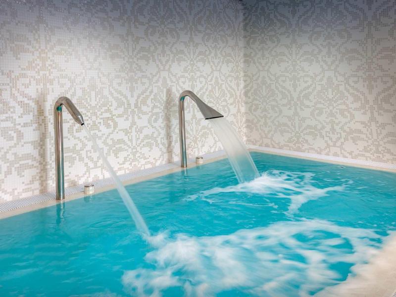 Indoor pool with water fountains flowing from two silver spouts into blue water.