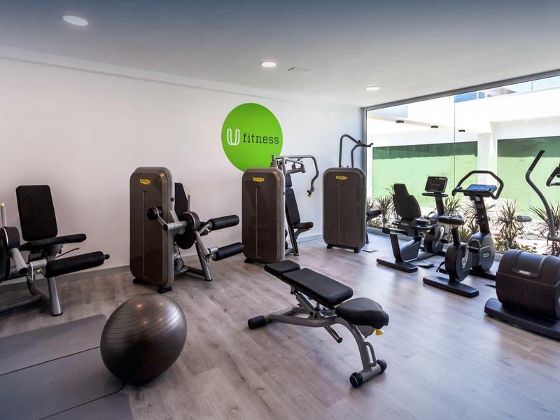 Modern gym with exercise machines, stationary bikes, and a workout bench in a bright room.