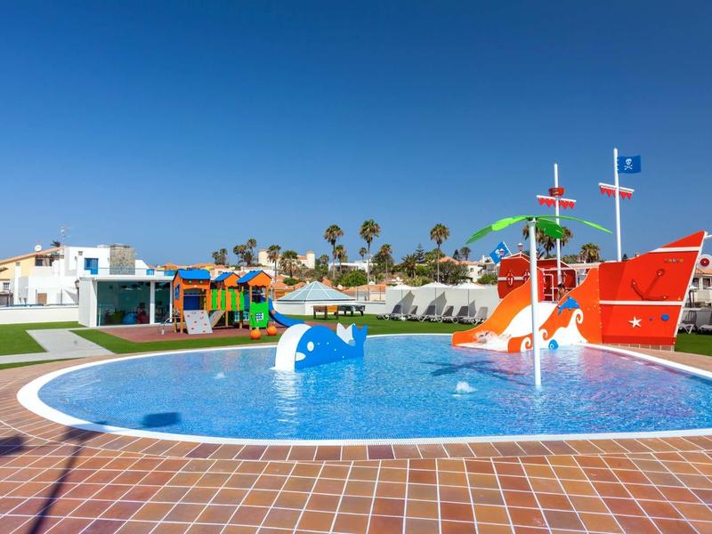 Outdoor kids' pool with colorful slides and water features under clear blue sky at a resort.