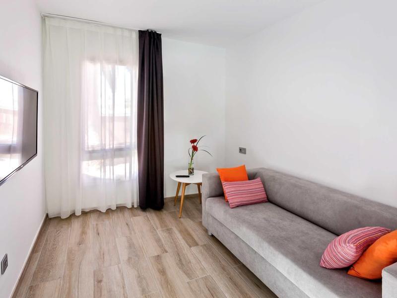 Small living space with gray sofa, colorful pillows, a round wooden table, and wall-mounted TV.