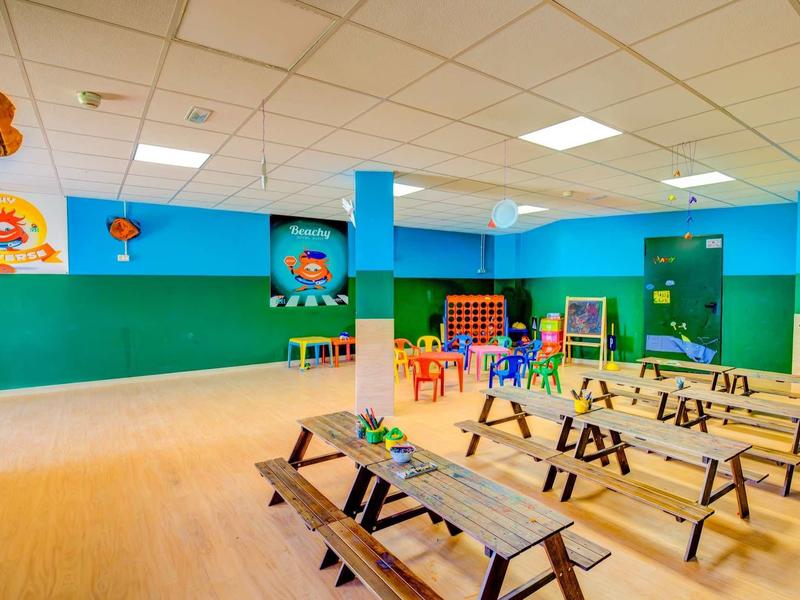 Ampia aula con sedie colorate, panchine e decorazioni adatte ai bambini.