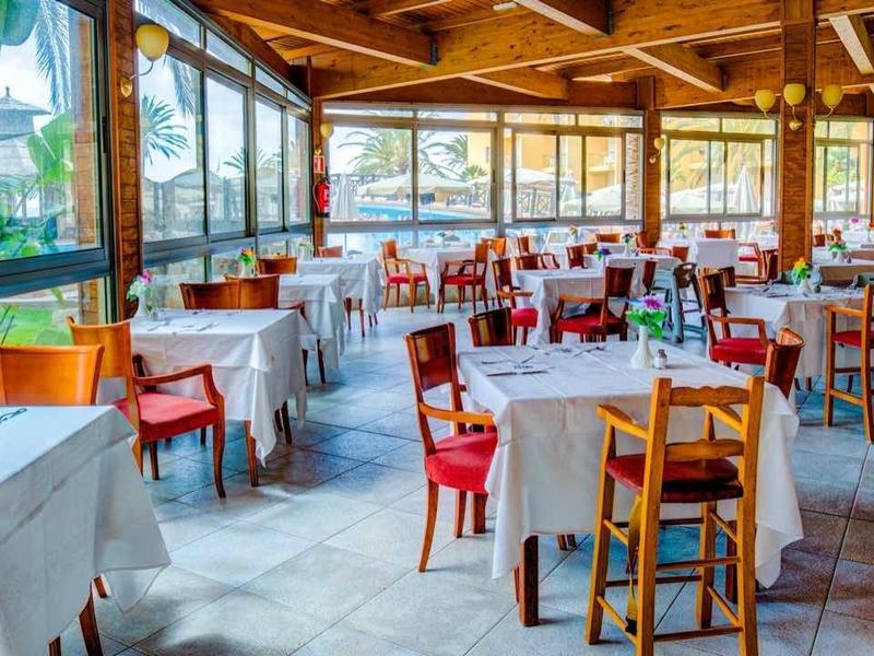 Ristorante luminoso con soffitto a travi in legno, grandi finestre e sedie rosse e bianche.