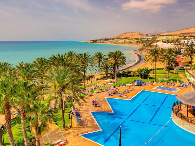 Vista di una piscina e palme vicino al mare in un resort tropicale.