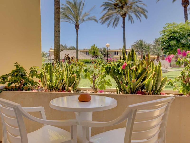 Piccolo balcone con tavolo e sedie bianchi, vista su giardino tropicale con palme.