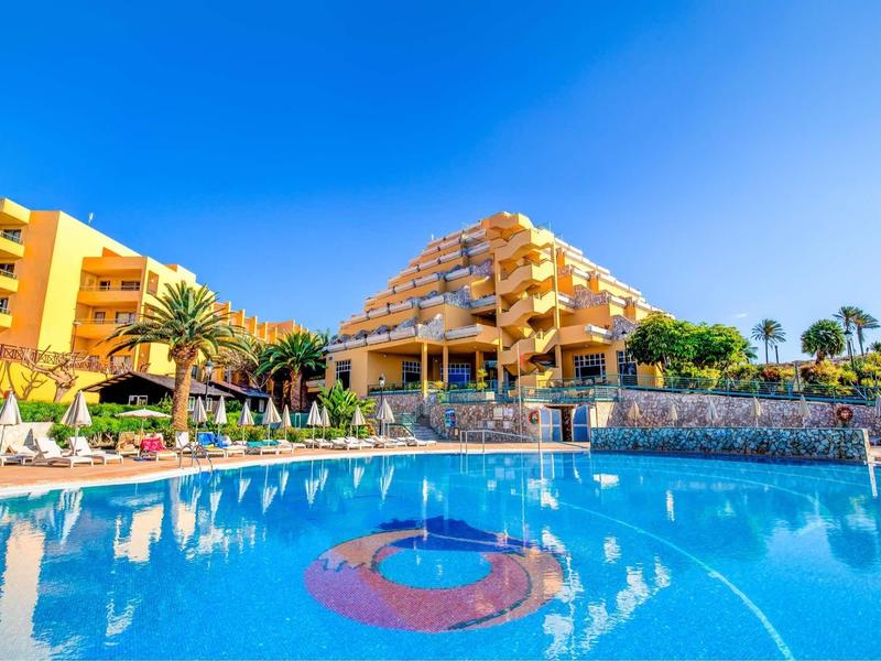 Hotel con architettura a terrazze e grande piscina all'aperto sotto un cielo sereno.