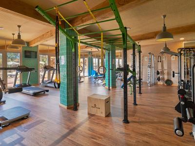 Gran gimnasio con suelo de madera, varias máquinas de entrenamiento y mucha luz natural.