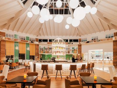Modern circular hotel bar area with central counter, wooden stools, and numerous hanging globe lights.