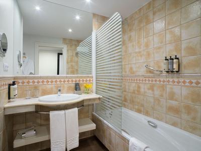 Modern bathroom with bathtub, glass shower screen, large mirror, and beige tiles.