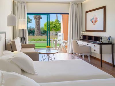 Modern hotel room with double bed, seating area, and view of terrace and garden.