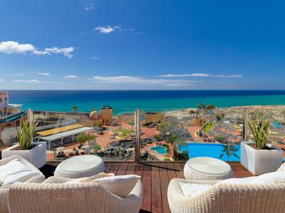 View from a terrace with white chairs overlooking the sea and beach under a blue sky.