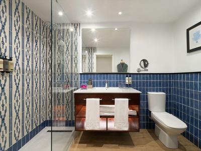 Modern hotel bathroom with blue tiles, glass shower, and double sink with towels.