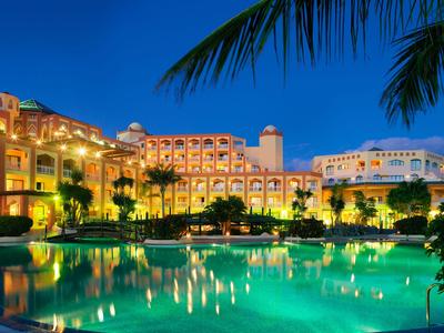 Illuminated hotel with large pool and palm trees at dusk