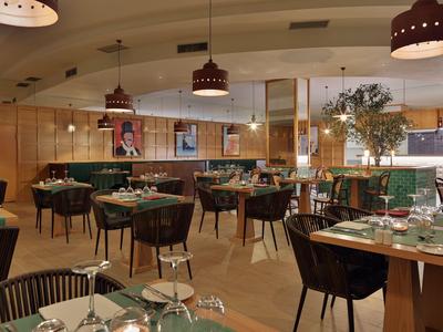 Modernly furnished hotel restaurant area with wooden walls, tables, and subdued lighting.