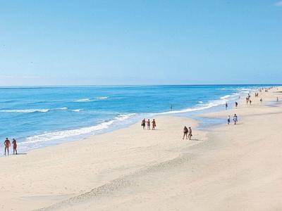 Ampia spiaggia sabbiosa con poche persone e mare calmo sotto cielo azzurro
