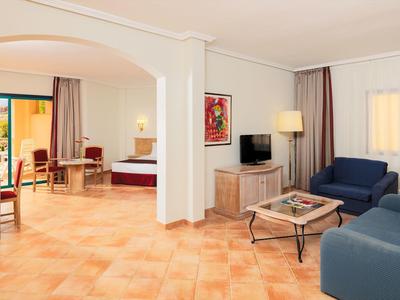 Suite d'hotel spaziosa con pavimento in cotto, divani blu e grande finestra con tende.