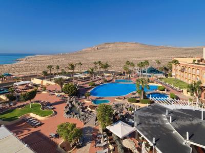 Resort con piscine blu, palme e spiaggia sotto un cielo limpido.
