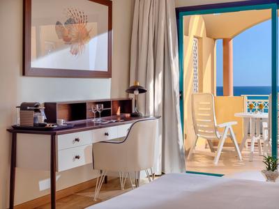 Camera d'hotel luminosa con scrivania, sedia e balcone con vista mare.