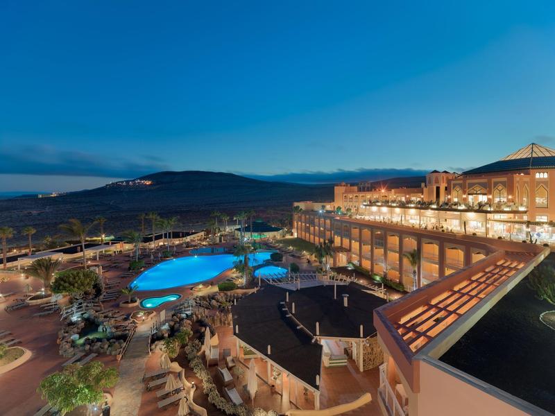 Resort con piscina illuminata e terrazza al crepuscolo sotto un cielo limpido.