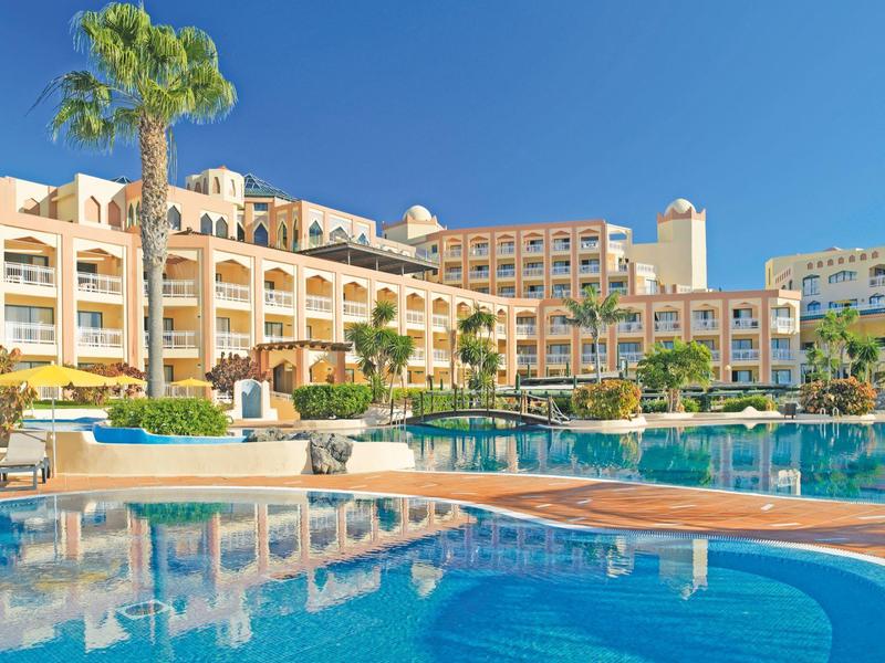 Un grande hotel con balconi accanto a una piscina azzurra sotto un cielo limpido.