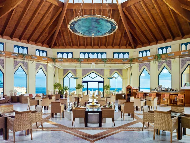 Ampia hall d'hotel con soffitto in legno, lucernario rotondo e grandi finestre che si affacciano sul verde.