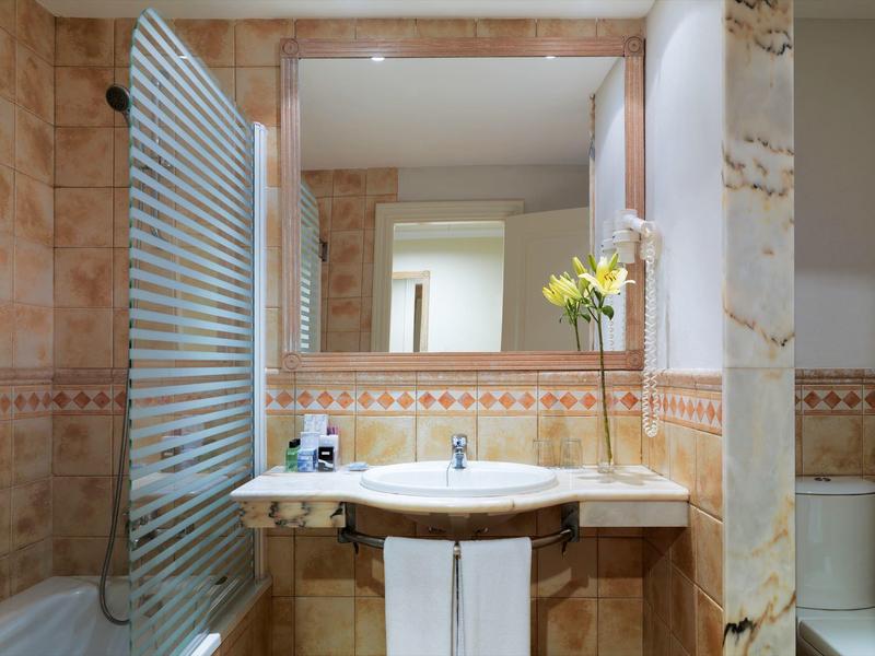 Bagno con pareti piastrellate beige, grande specchio, lavabo e parete doccia in vetro a strisce.